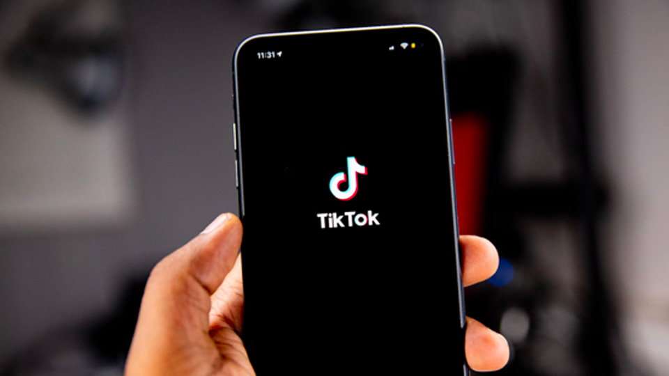 A hand holds an iPhone with the TikTok loading screen on display